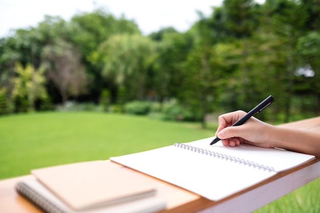 Closeup image of a hand writing on a notebook in the outdoors