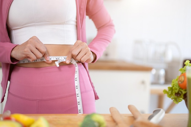 Closeup image of a healthy and slim woman in sportswear measuring her waist with a measuring tape
