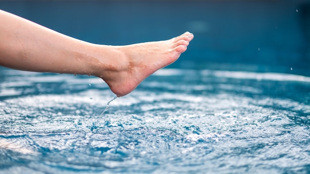 Closeup image of legs and barefoot kicking and splashing water in the pool