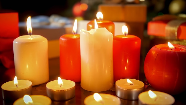 Closeup image of lots of white and red burning candles on wooden table at living room