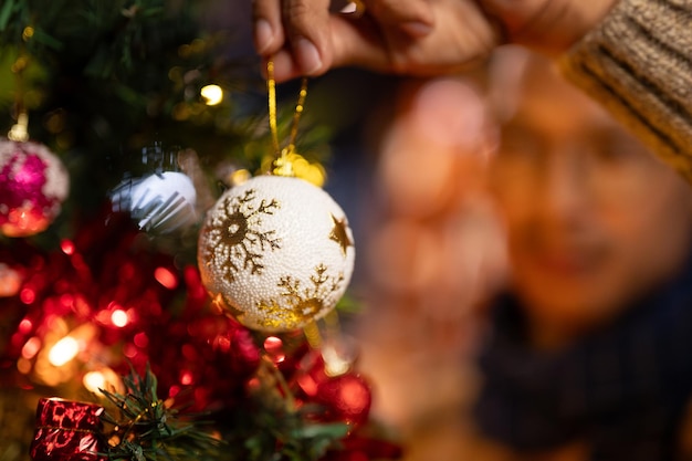 Closeup image of a man hanging a Christmas ball ornament on a Christmas tree in the living room