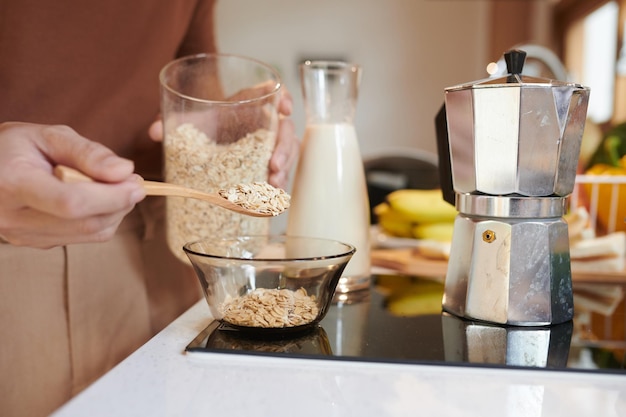 Closeup image of man putting several spoons of oat flakes in bowl