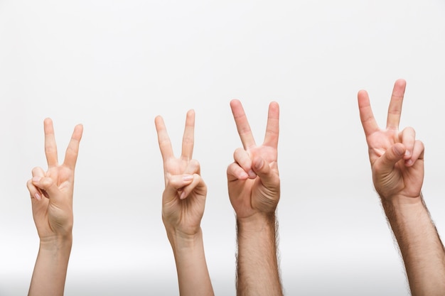 Photo closeup image of a man's and woman's raised hands isolated over white wall wall showing peace gesture.