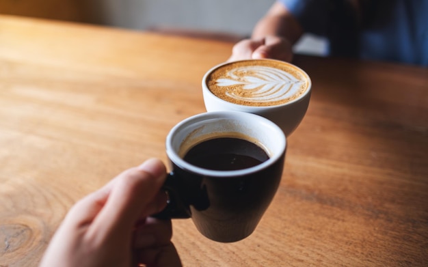 Closeup image of a man and a woman clinking white coffee mugs in cafe