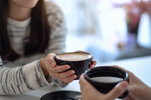 Closeup image of a man and a woman holding two coffee cups together