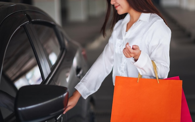 Фото Крупным планом изображение красивой женщины, держащей хозяйственные сумки, открывая дверь автомобиля на стоянке торгового центра