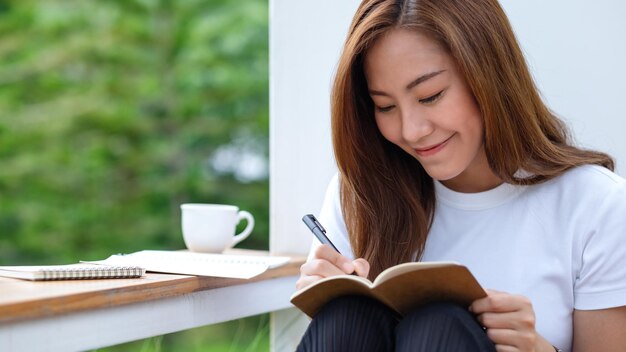 写真 屋外でノートに書いている美しい若いアジアの女性のクローズアップ画像