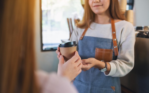 写真 店で顧客にコーヒーの紙コップを保持し、提供しているウェイトレスのクローズアップ画像