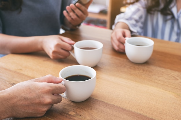 Крупным планом изображение людей, использующих мобильный телефон и пить кофе вместе