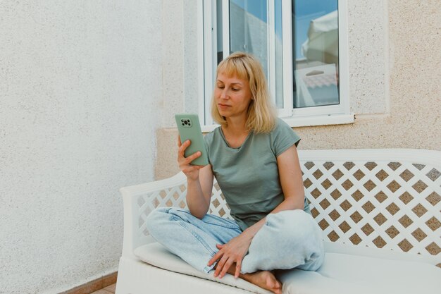 Closeup image of pretty woman sitting at cozy home interior and using modern smartphone device female hands typing text message via cellphone social networking concept