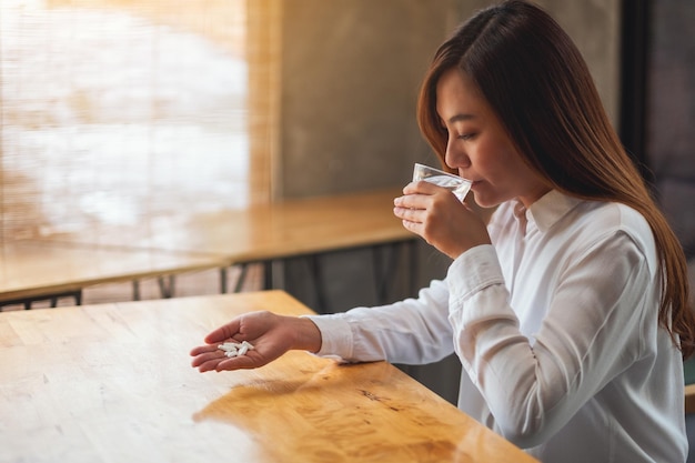 Closeup image of a sick woman holding a white pills while taking medicine and drinking water