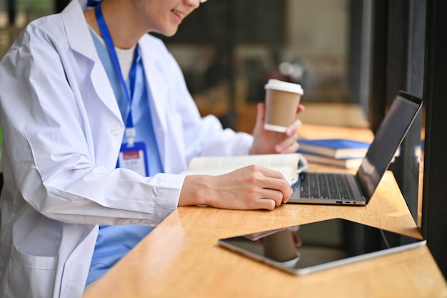 Closeup image of a smart asian male doctor reading a book and sipping coffee at a cafe