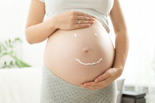 Крупным планом изображение знака улыбки, нарисованного кремом на животе беременной