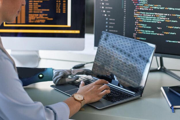 Closeup image of software developer with bionic arm working on\
laptop creating new application