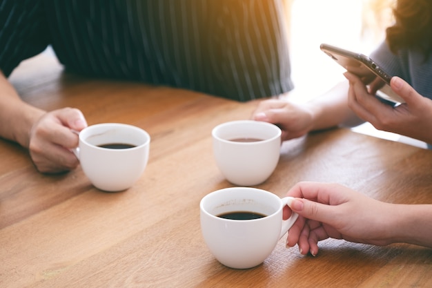 木製のテーブルで飲むためにコーヒーカップを保持している3人のクローズアップ画像