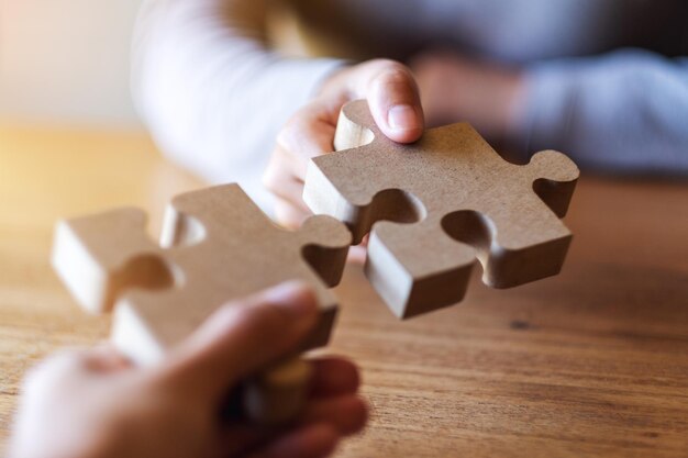 Closeup image of two people holding and putting a piece of wooden jigsaw puzzle together