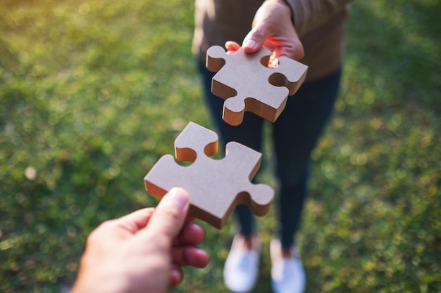 Closeup image of two people holding and putting a piece of wooden jigsaw puzzle together