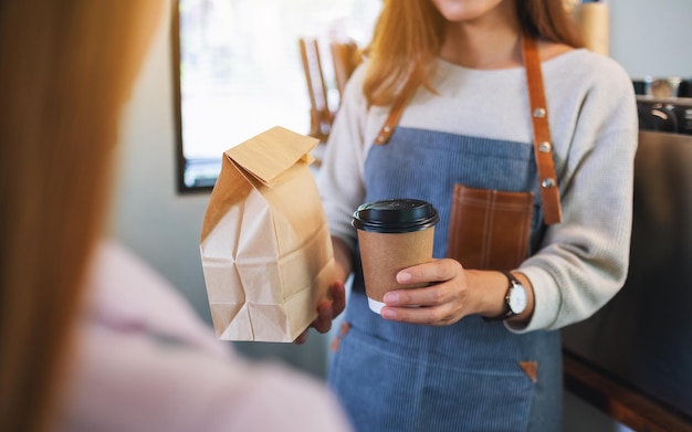 Closeup image of a waitress holding and serving paper cup of coffee and takeaway food in paper bag to customer in a shop