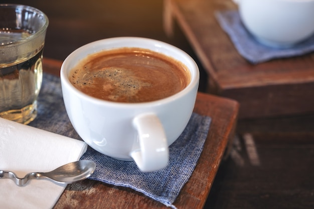 Closeup image of a white cup of hot coffee and a glass of tea on vintage wooden table in cafe