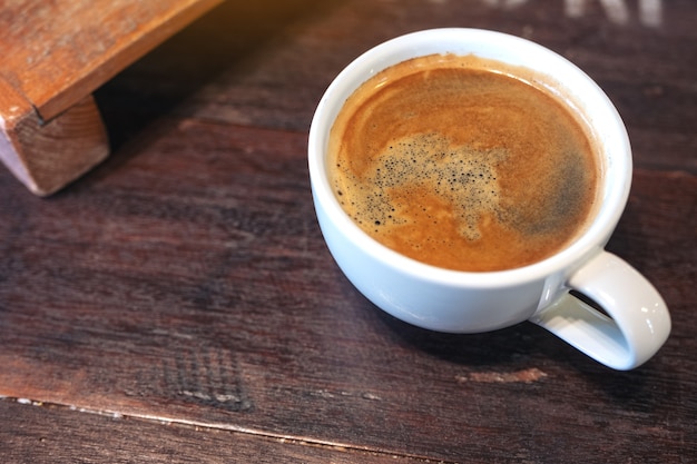 Immagine del primo piano di una tazza bianca di caffè caldo sulla tavola di legno d'annata nella caffetteria