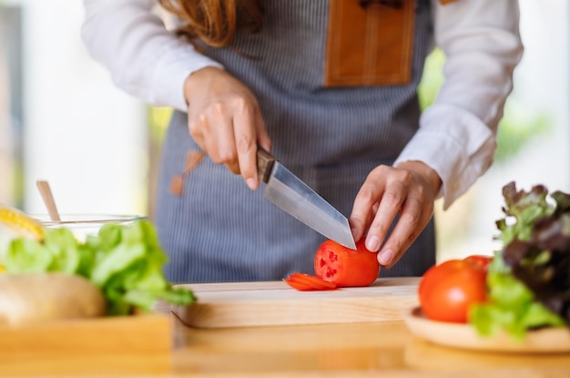 Immagine del primo piano di una donna chef che taglia e trita il pomodoro con un coltello su una tavola di legno