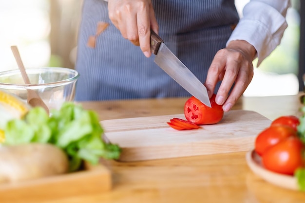 나무 판자에 칼로 토마토를 자르고 자르는 여성 요리사의 근접 촬영 이미지