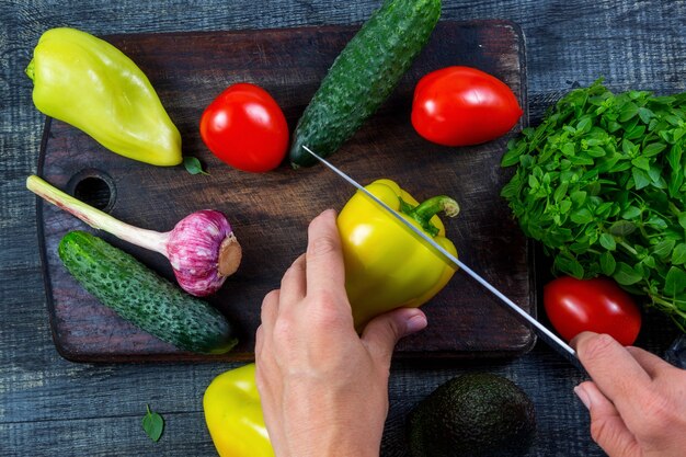 Closeup image of a woman cutting and chopping bell pepper by knife on wooden board