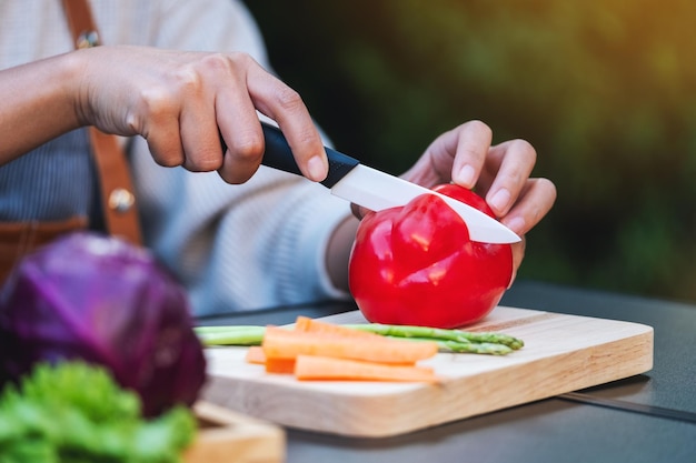 トレイに野菜を混ぜた木の板にナイフで赤いベルペッパーを切って切り刻む女性のクローズアップ画像