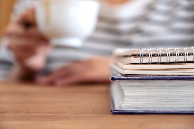 Closeup image of a woman drinking coffee with books and notebooks on wooden table