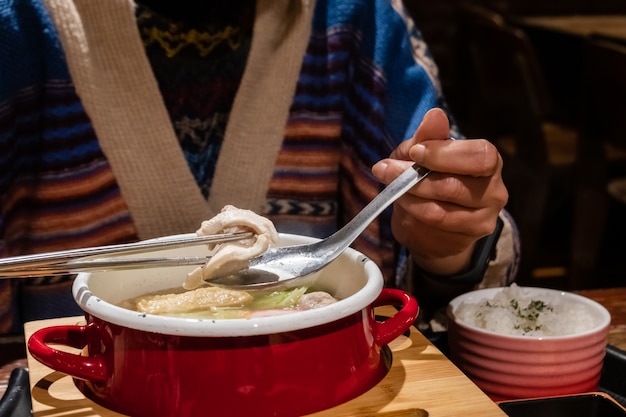 Immagine del primo piano di una donna che mangia una pentola calda con verdure e carne di maiale