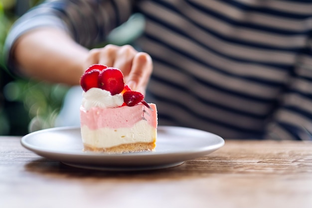 Closeup image of a woman eating a strawberry cheese cake in a plate