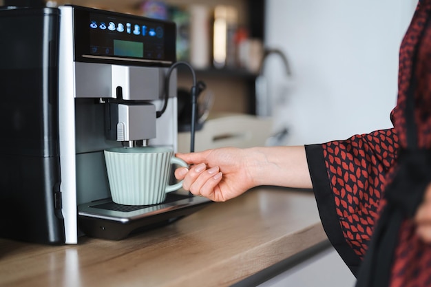 自宅でコーヒーの大きなマグカップを作るときにコーヒーマシンを使用して女性の手のクローズアップ画像