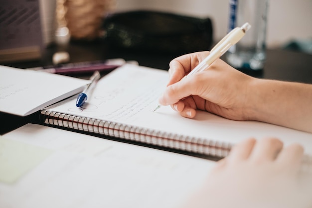 Closeup image of a woman hand writing on a notebook doing homework during university preparing for exam with textbook and taking notes selective focus on the pencil