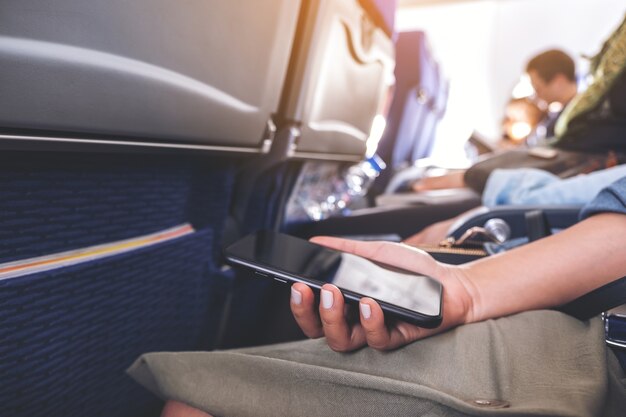 Closeup image of a woman holding a black smart phone while sitting in the cabin