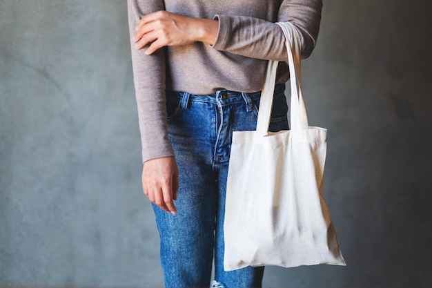 Closeup image of a woman holding and carrying a white fabric tote bag for reusable and environment concept