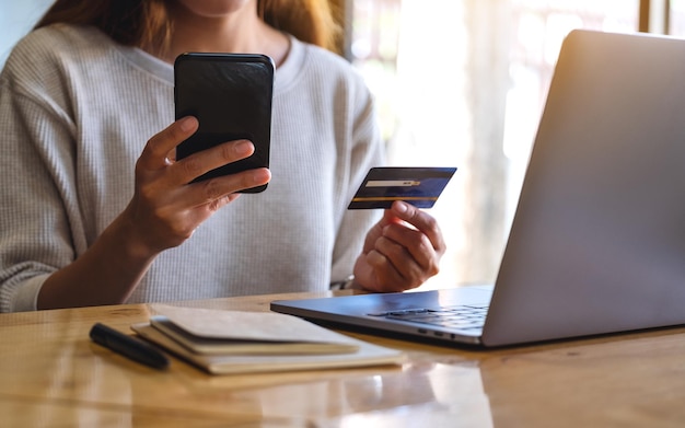 Closeup image of a woman holding credit card while using smart phone and laptop in office