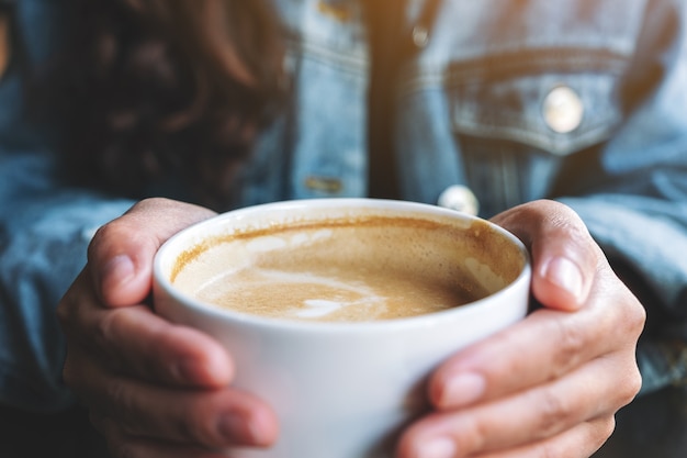 Closeup image of a woman holding a cup of hot latte coffee on the table