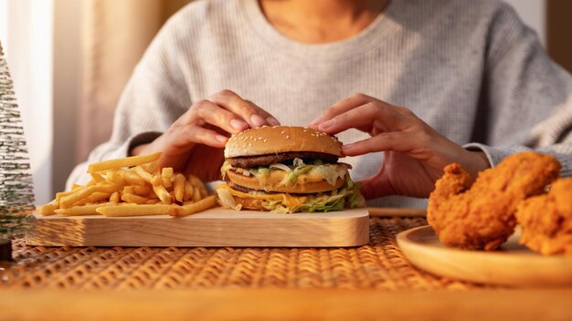 自宅のテーブルにフライドチキンとハンバーガーとフライドポテトを持って食べている女性のクローズアップ画像