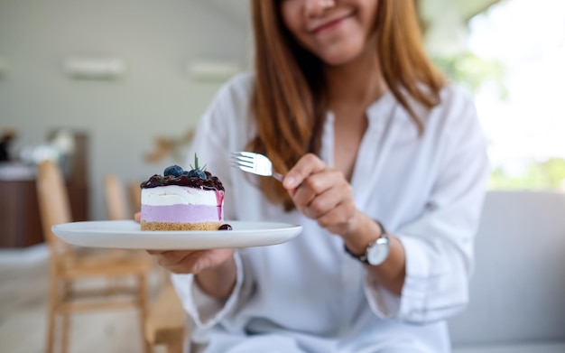 Closeup image of a woman holding and eating a piece of blueberry cheesecake