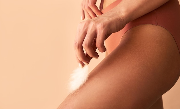 Closeup image of a woman holding a feather on her legSmooth skin depilation