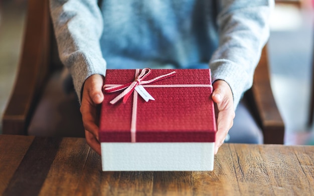 Closeup image of a woman holding and giving a red gift box