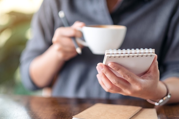Closeup image of a woman holding notebook and coffee cup to drink on the table