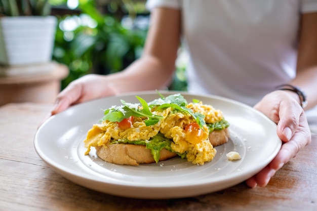 Closeup image of a woman holding a plate of scrambled eggs and avocado open sandwich