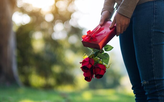 Closeup image of a woman holding red roses flower and a gift box in the park