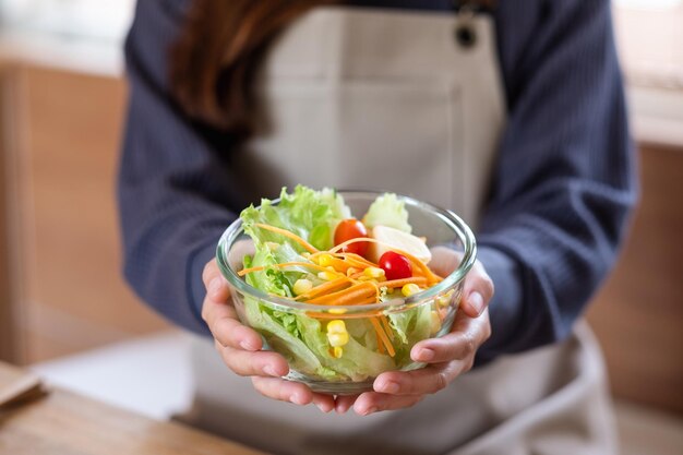 Closeup image of a woman holding and showing a fresh mixed vegetables salad in the kitchen at home