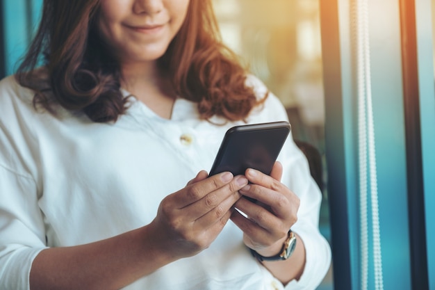 Closeup image of a woman holding , using and looking at smart phone in cafe