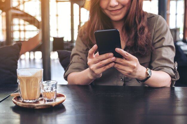 Closeup image of a woman holding , using and looking at smart phone with coffee cup on wooden table