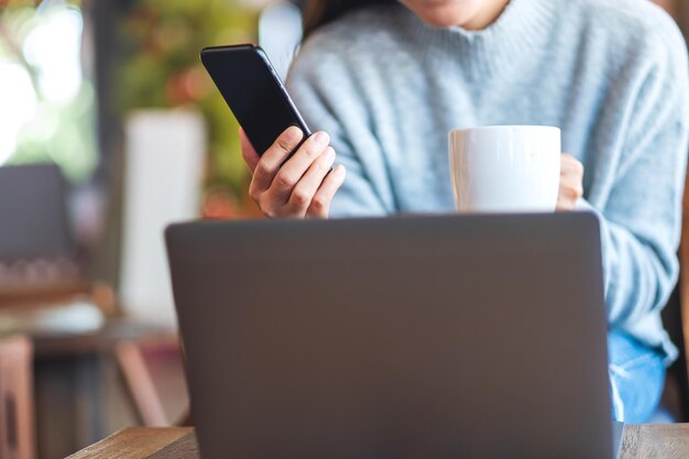 Closeup image of a woman holding and using mobile phone and laptop computer in cafe