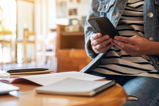 Photo closeup image of a woman holding and using smart phone while working on paper