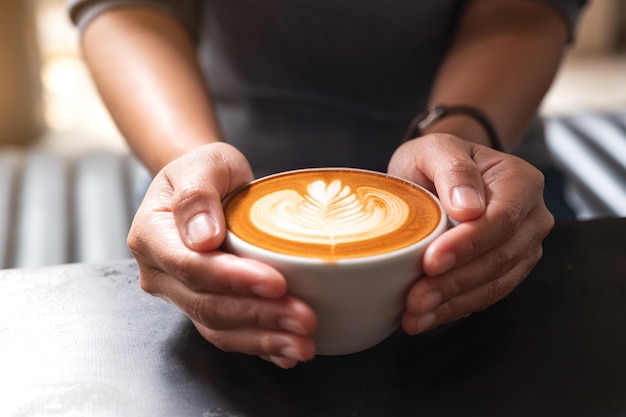 Closeup image of a woman holding a white cup of coffee with latte art